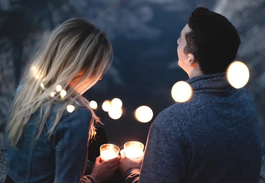 Woman and man holding candles under string lights at night